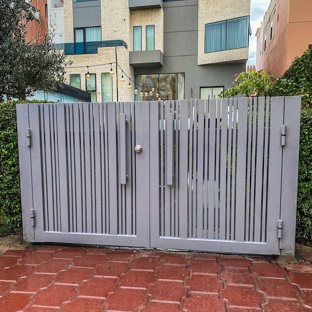 Wide alternate-angle view of a modern steel slatted driveway gate