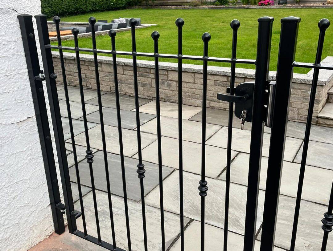Traditional black spear-top steel gate and matching railing on a garden wall