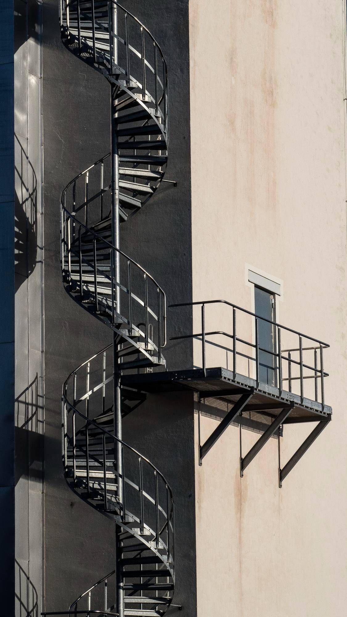 External spiral steel fire escape staircase with cantilevered exit landing on a modern building facade