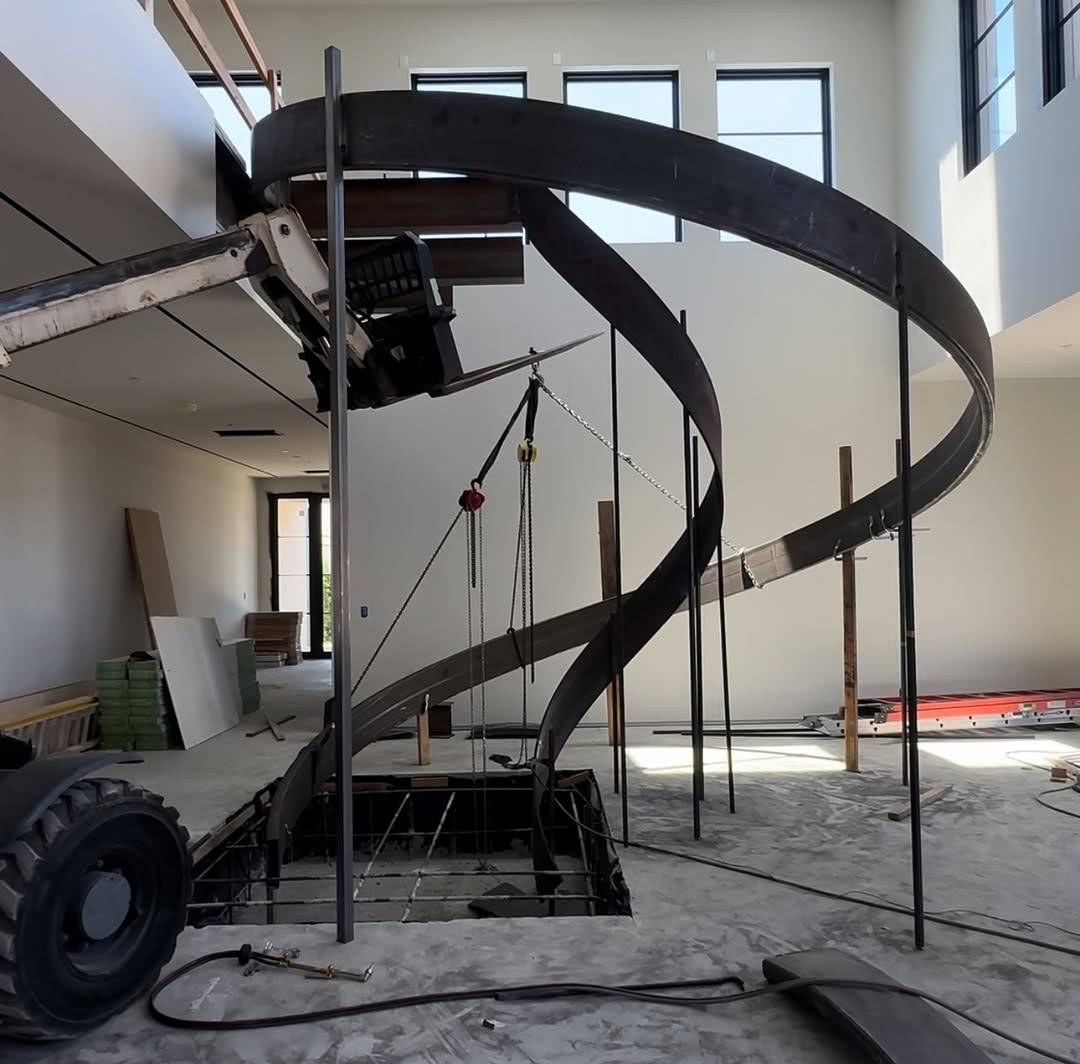 bare curved steel helical staircase frame being lifted into position before treads are fitted