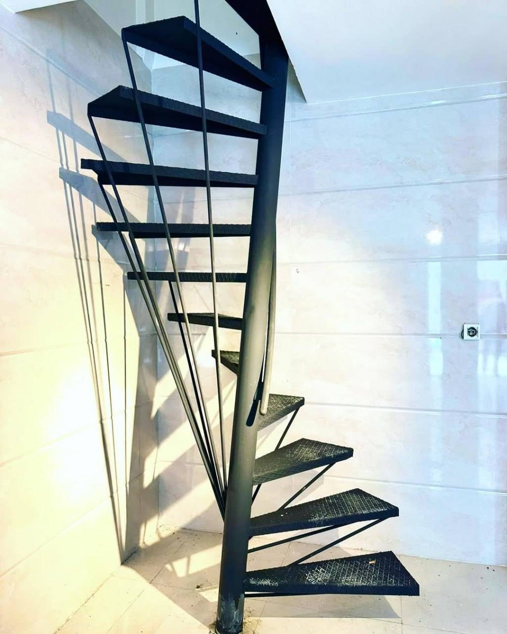 Black steel spiral staircase with central column in a bright minimalist room
