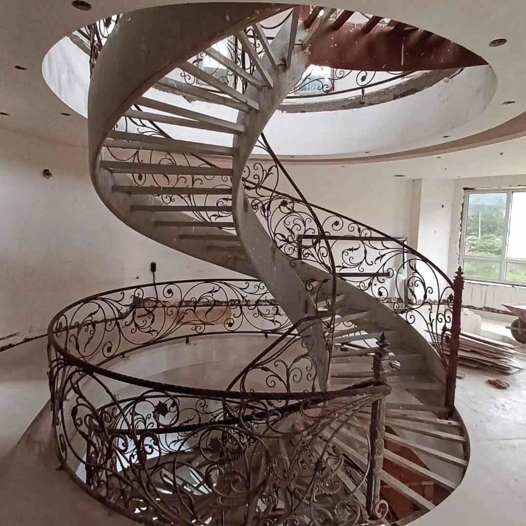 Heritage restoration of an ornate wrought-iron helical staircase with scrollwork balustrade under a skylight