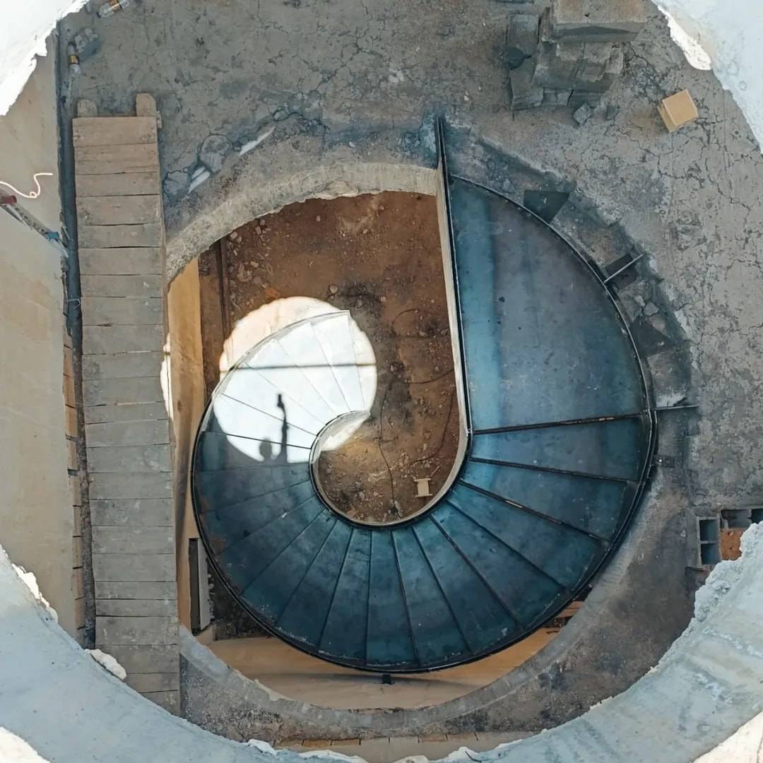 aerial view of a helical staircase descending into a construction pit, second staircase visible in background