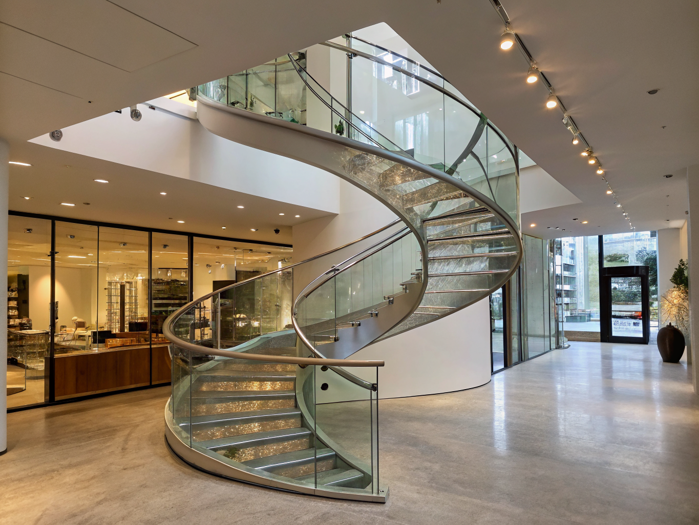 Steel-tread spiral staircase with curved glass balustrade in an open-plan glass-walled living space
